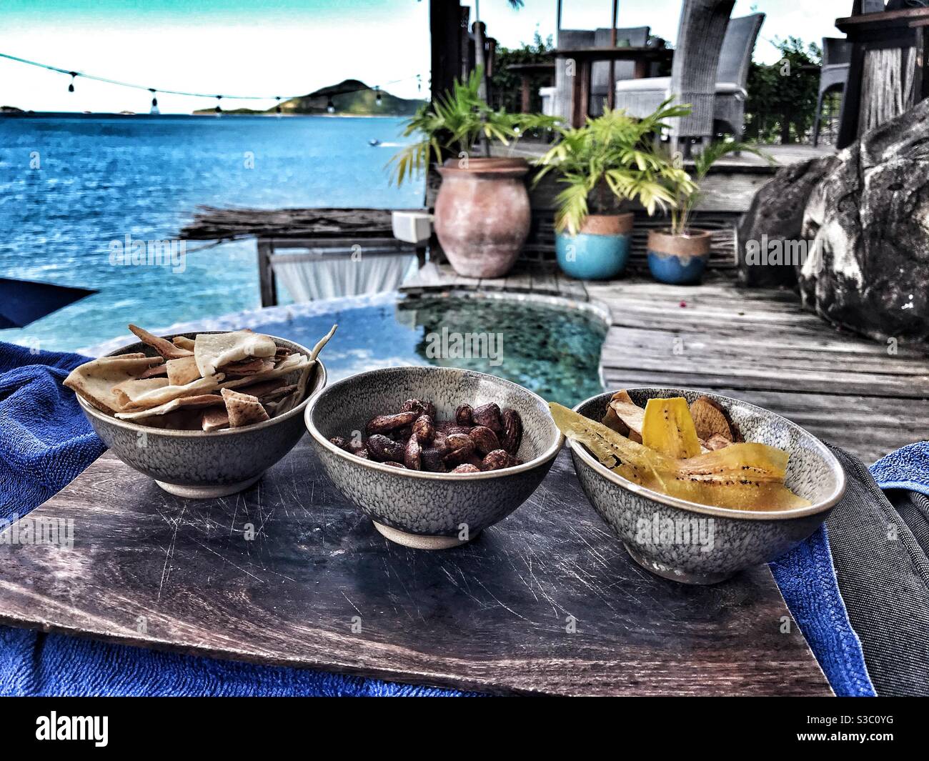 3 bowls of Tapas on a wooden board overlooking a plunge pool and Caribbean Sea at Sheer Rocks in Antigua Stock Photo