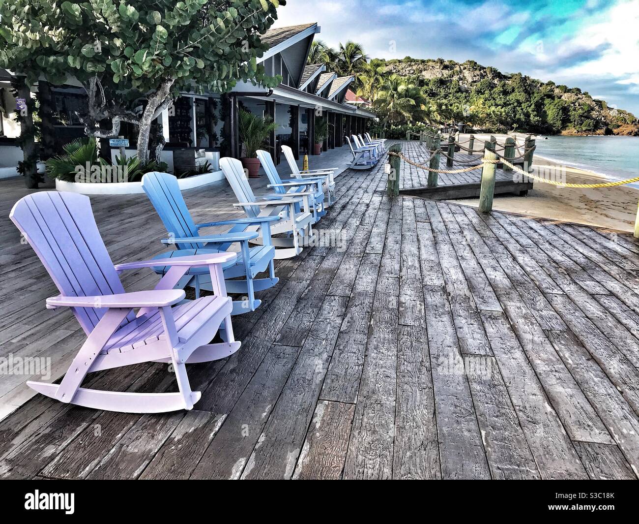 A row of Adirondack chairs in Pink and Blue lined up on decking overlooking the Caribbean Sea at Galley Bay Resort and Spa in Antigua - Smartphone Captured Stock Image