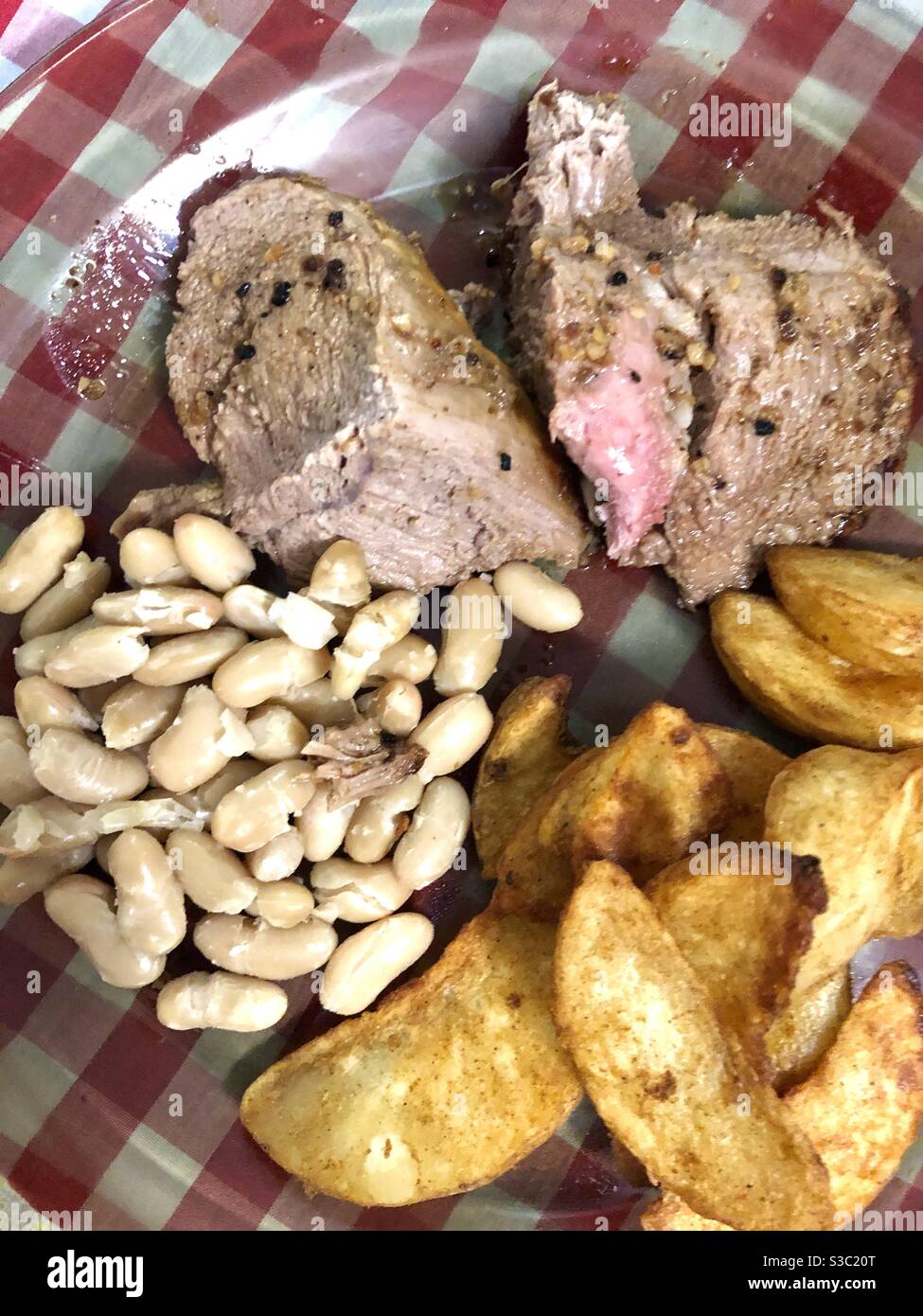 Lamb meat with beans and potatoes wedges in a see through plate. - Smartphone Captured Stock Image