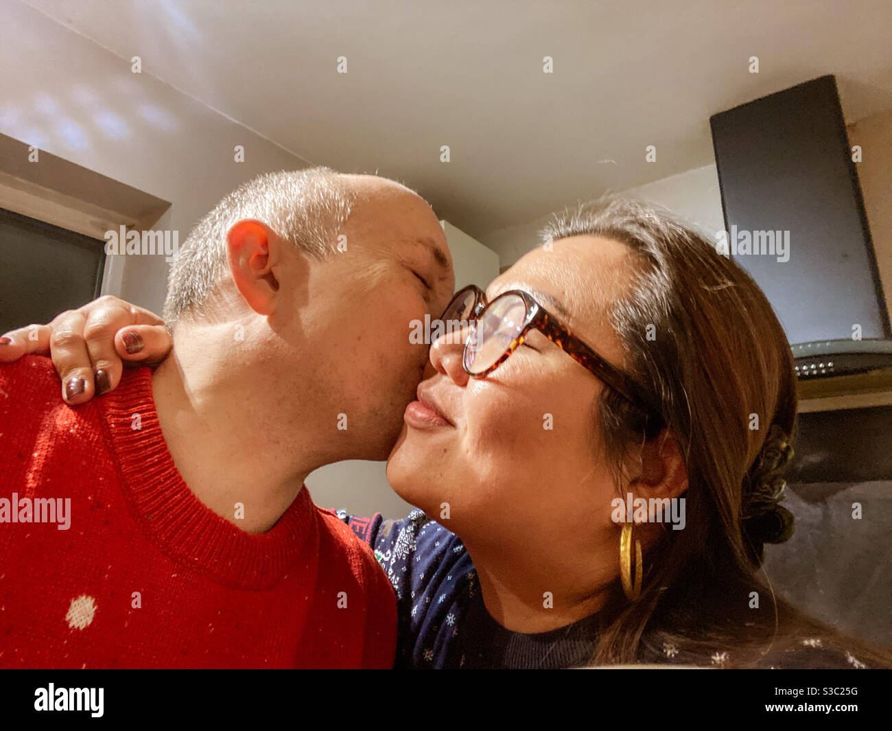 A mixed race couple share a kiss on the cheek. - Smartphone Captured Stock Image