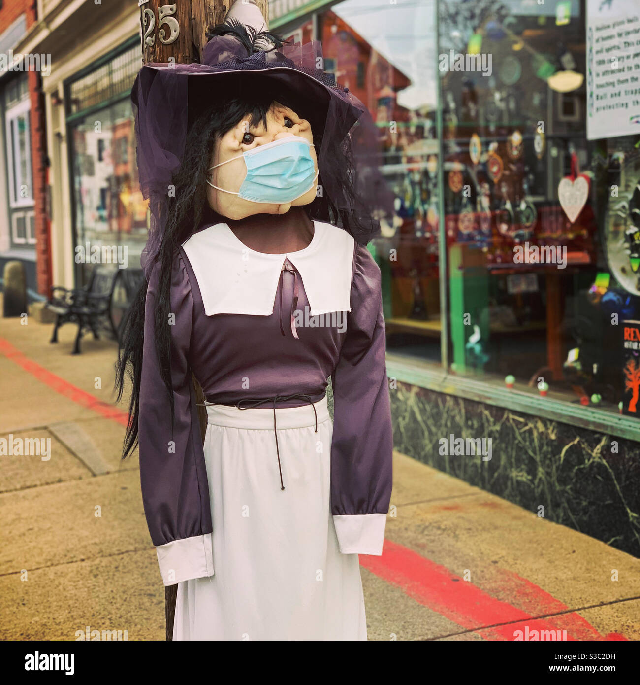 Salem, Massachusetts, United States. December, 2020. A witch decoration on a sidewalk, wearing a face mask. - Smartphone Captured Stock Image