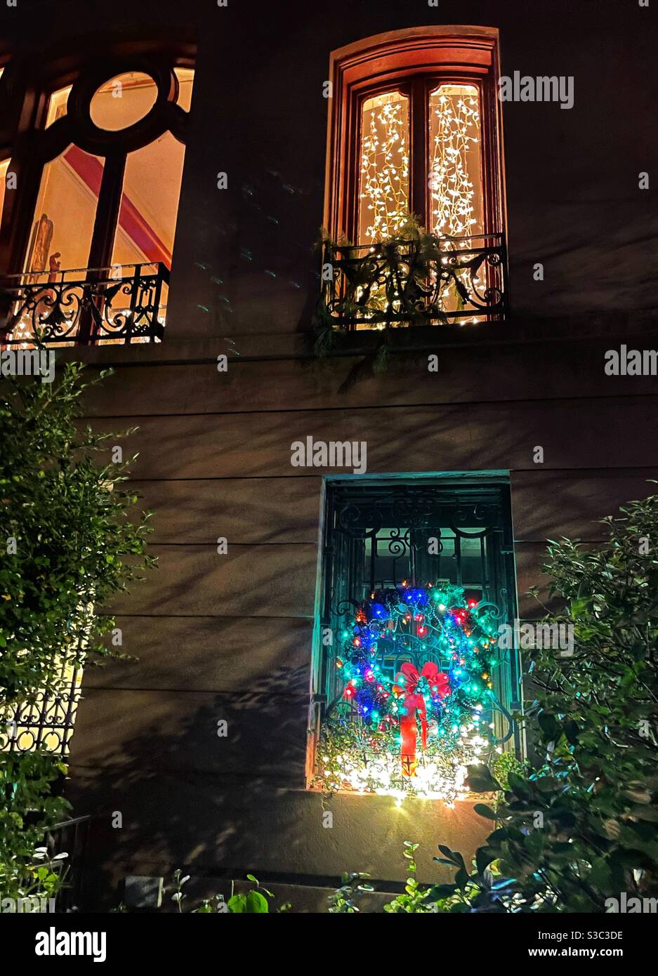 The warm glow of Christmas lights twinkling in elaborate arched windows of a luxury brownstone in Manhattan brighten the streets of the city - Smartphone Captured Stock Image