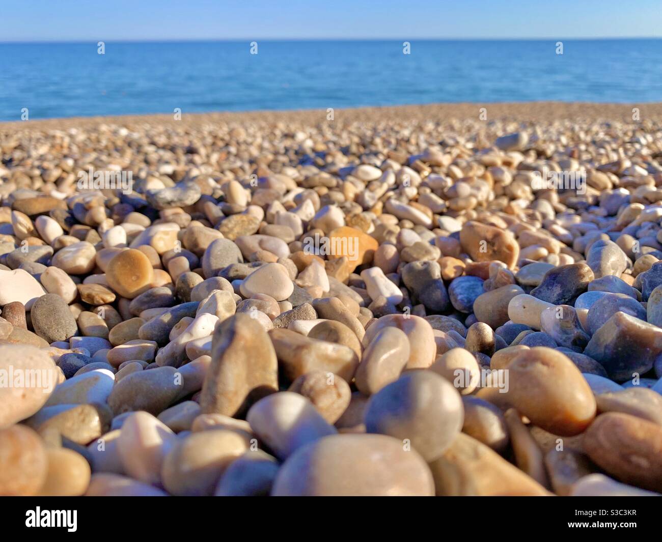 Close-up of colourful pebbles in the foreground on Weston beach, Devon, England on bright summer day with the blue sea in background Stock Photo