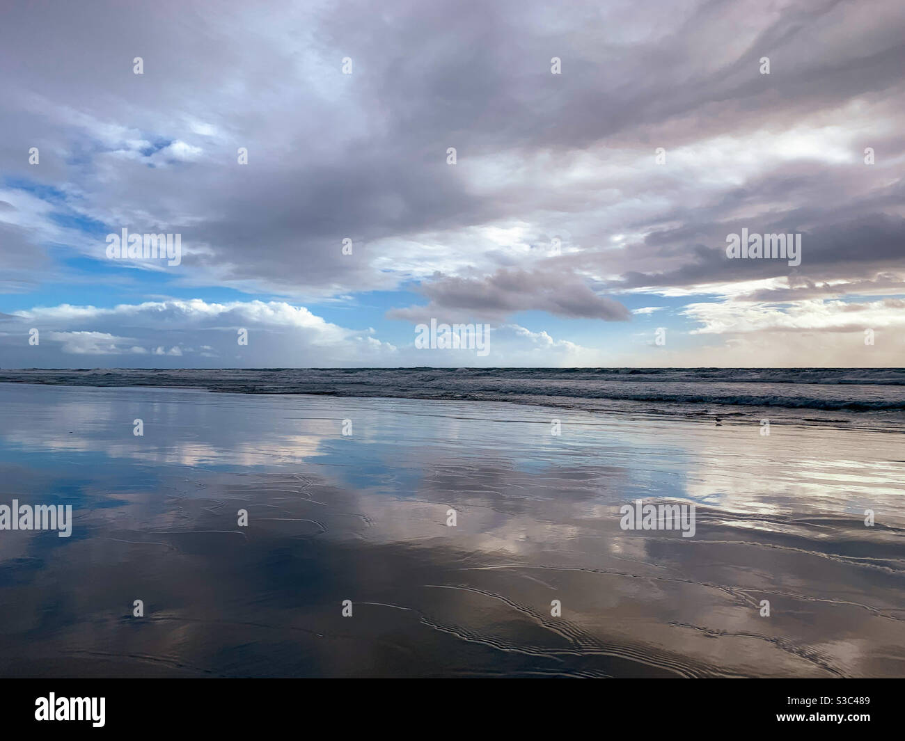 Dramatic cloudscape reflecting on wet sand on beach. - Smartphone Captured Stock Image