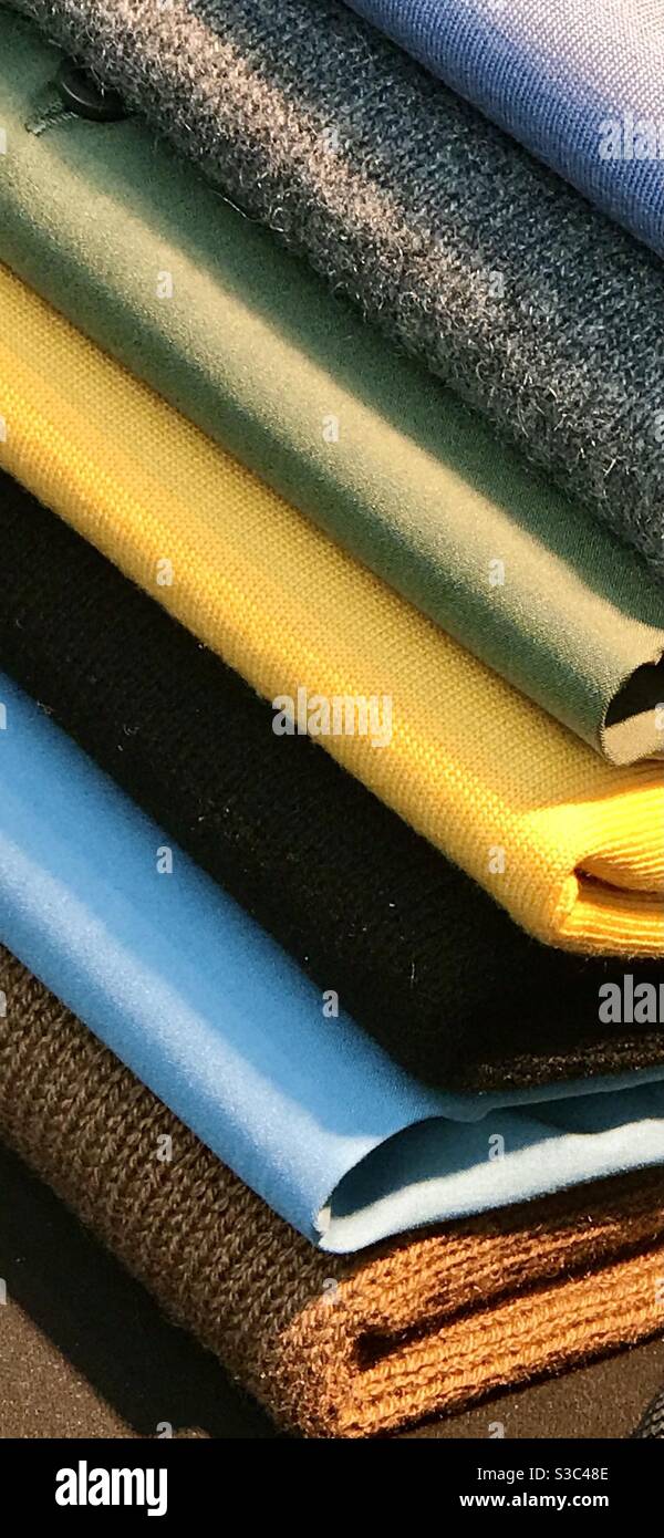 A pile of folded sweaters, knitted in different colours and weights.  Yellow, blue, olive, grey, charcoal and ochre. Stock Photo
