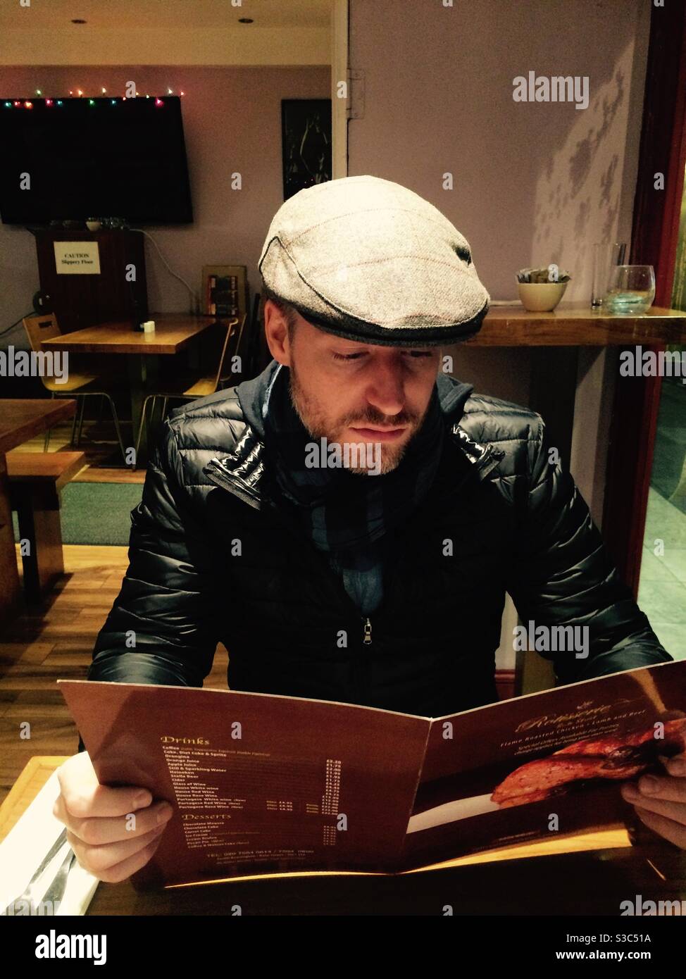 Young man in a cap reading a menu in a restaurant in Kensington Stock Photo