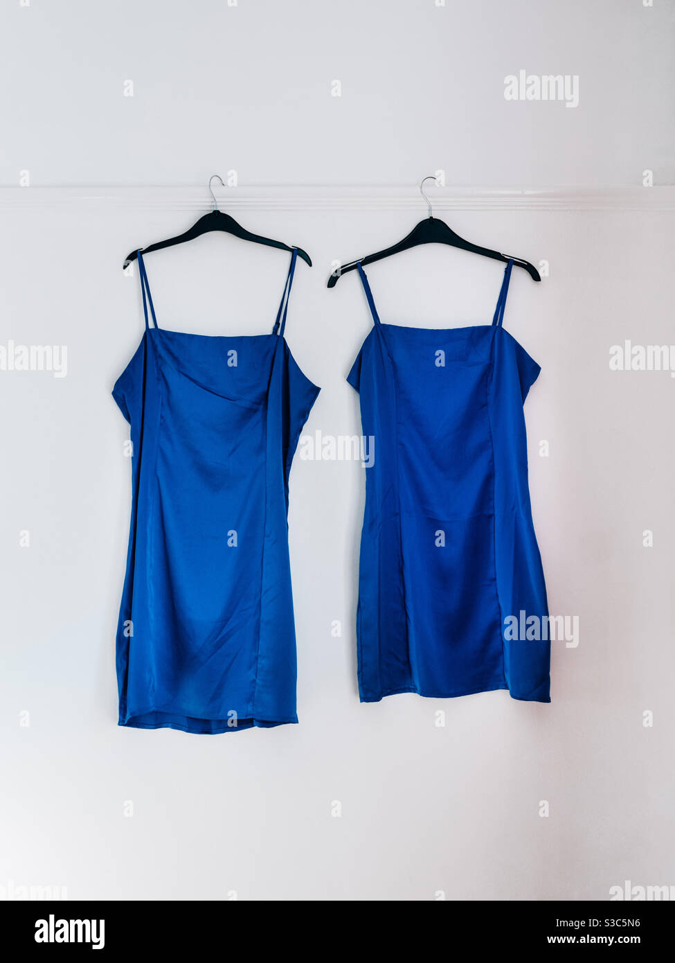Matching blue satin dresses on hangers against a white wall Stock Photo