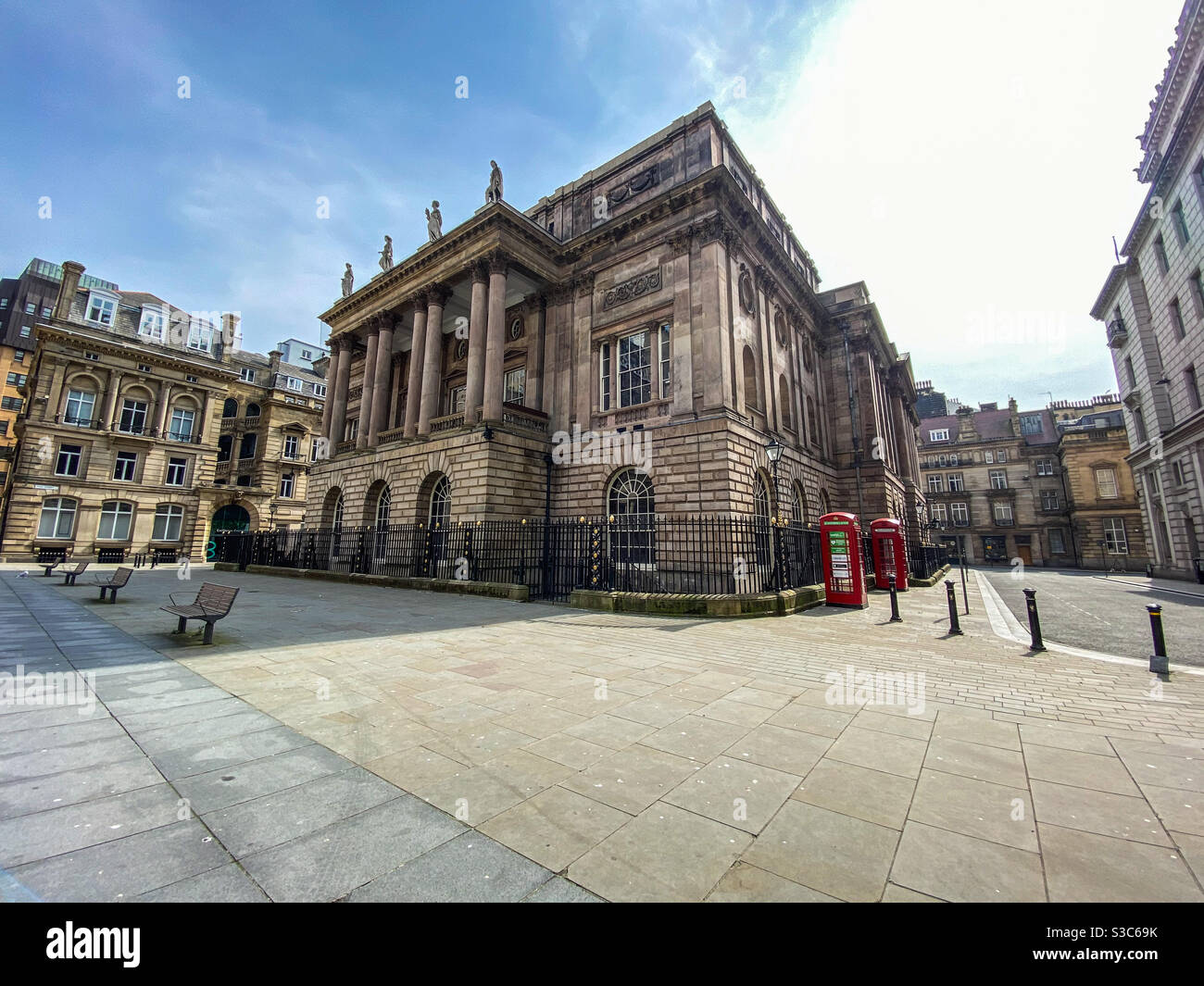 Liverpool town hall taken from exchange flags with no people around due to the coronavirus pandemic outbreak lockdown. There is empty benches & two iconic British red telephone boxes on the street Stock Photo