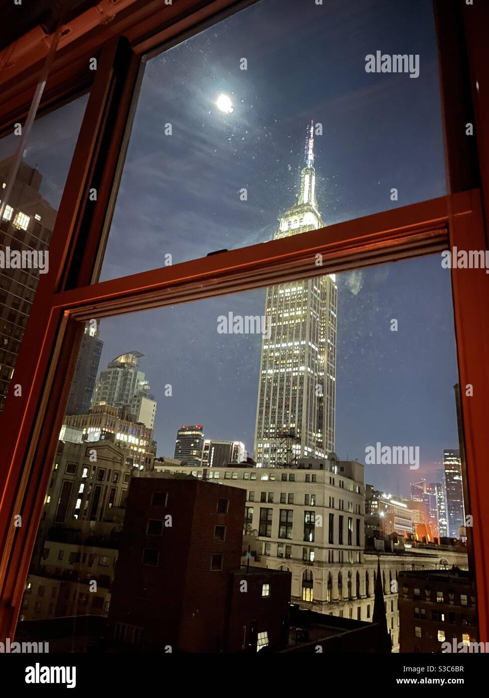 A room with a view! A beautiful view of the lit up Empire State building and the full moon on a winters night in Midtown Manhattan, New York, USA - Smartphone Captured Stock Image