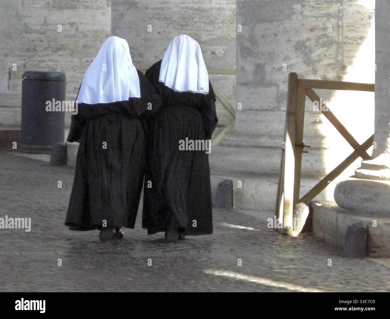 Two nuns in black and white dress walk towards a bin in Rome, Italy Stock Photo