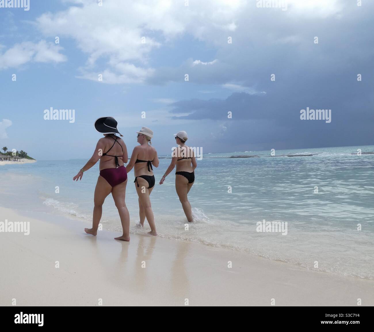 Three women walking along the shoreline at at beach in Mexico. They are all wearing bikinis & sun hats Stock Photo