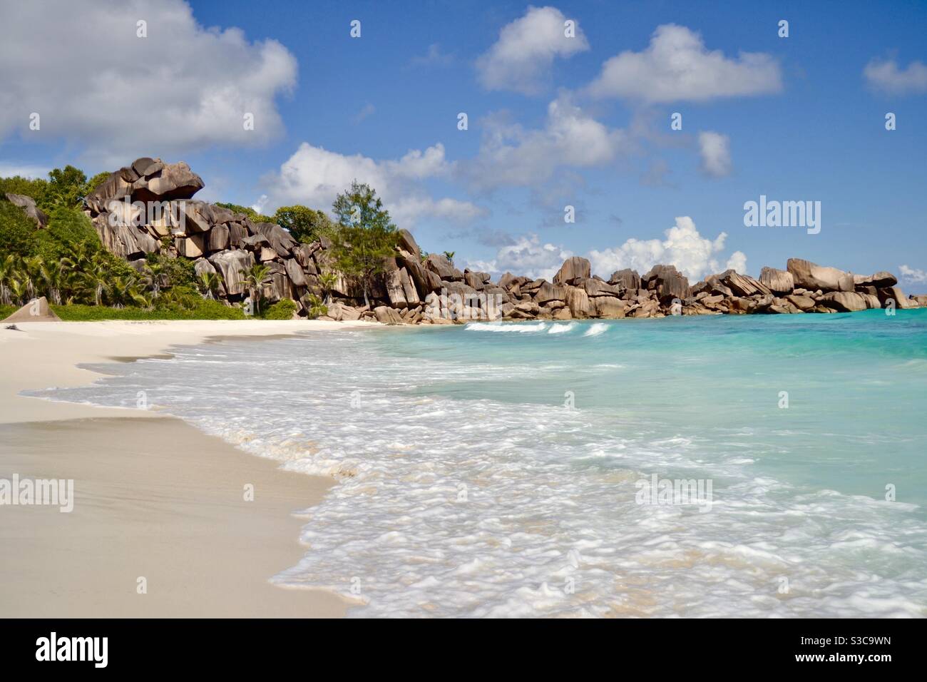 Soft waves of the crystal clear turquoise Indian Ocean lap at pure white sand OL along the beach on the luxury island of La Digue, part of the Seychelles archipelago of paradise Stock Photo