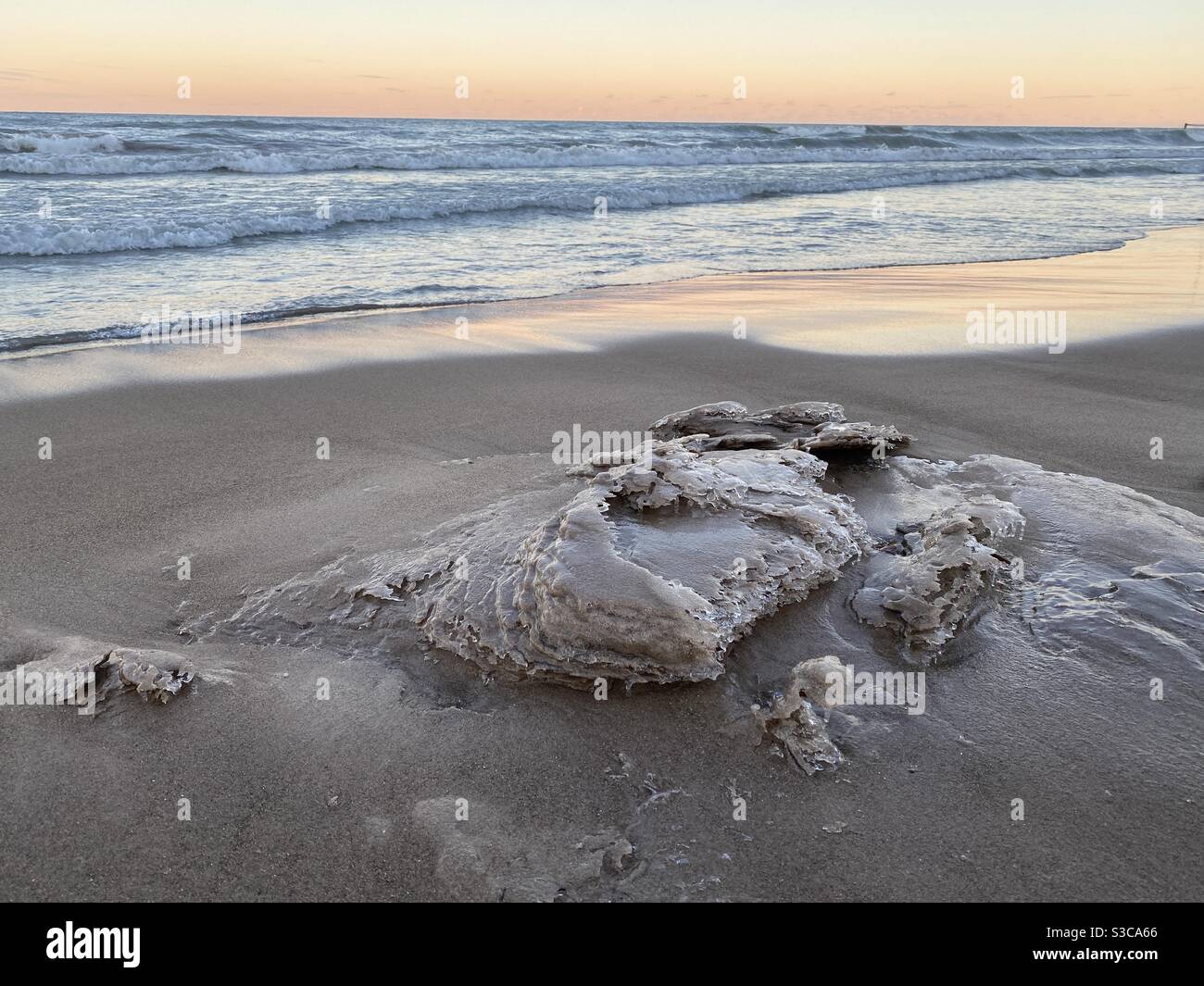 Winter waves leave icy sand sculptures on Lake Michigan beach. Sunset at Gillson Beach on the lake’s Illinois shore. Stock Photo