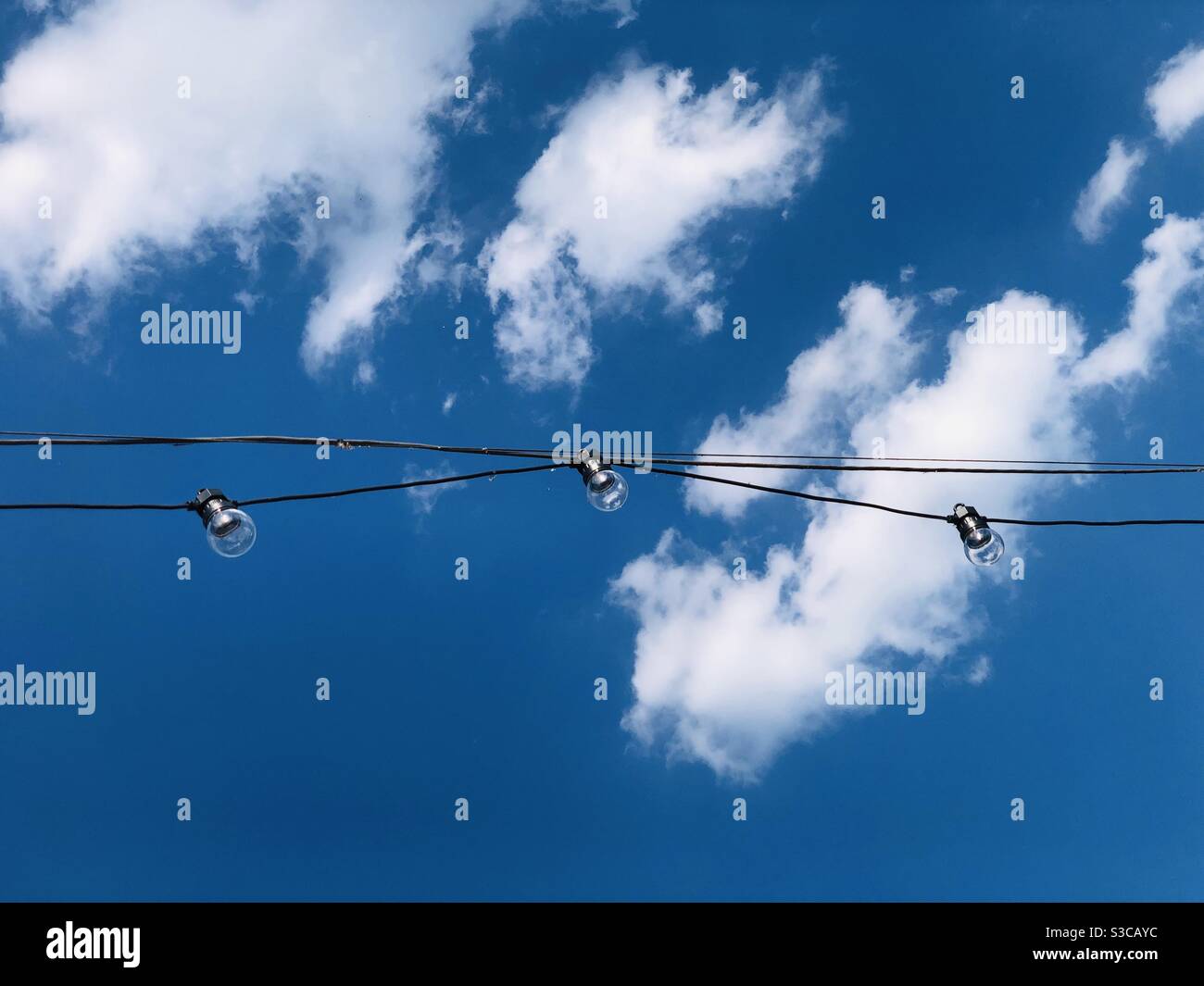 Looking up at hanging lightbulbs against blue sky - Smartphone Captured Stock Image