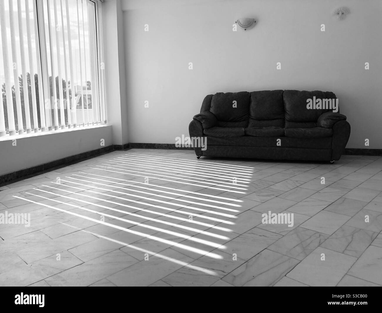 Monochromatic photo of a minimalist room with one sofa and shadows reflecting on the floor Stock Photo