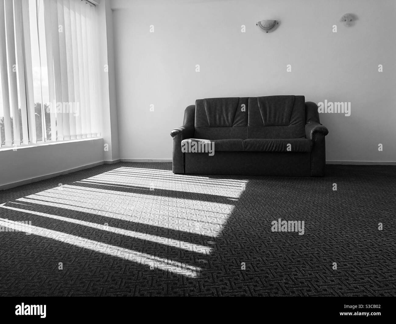 Monochromatic photo of a minimalist room with one sofa and shadows reflecting on the floor Stock Photo