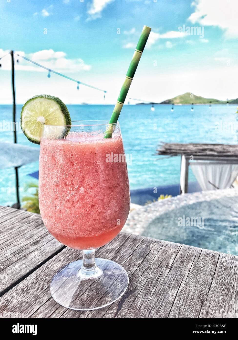 Strawberry Daiquiri Cocktail with a Garnish of Lime and a paper straw on a table with the Caribbean Sea of Antigua and a plunge pool in the view behind - Smartphone Captured Stock Image