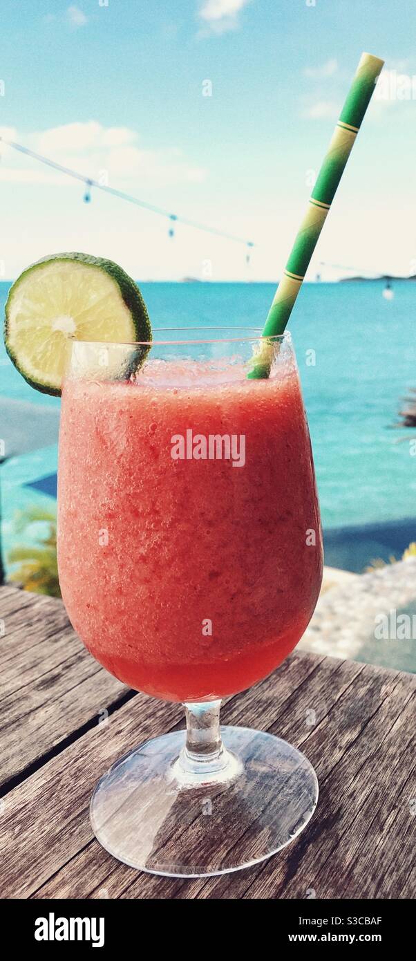 Strawberry Daiquiri Cocktail with a Garnish of Lime and a paper straw on a table with the Caribbean Sea of Antigua behind Stock Photo