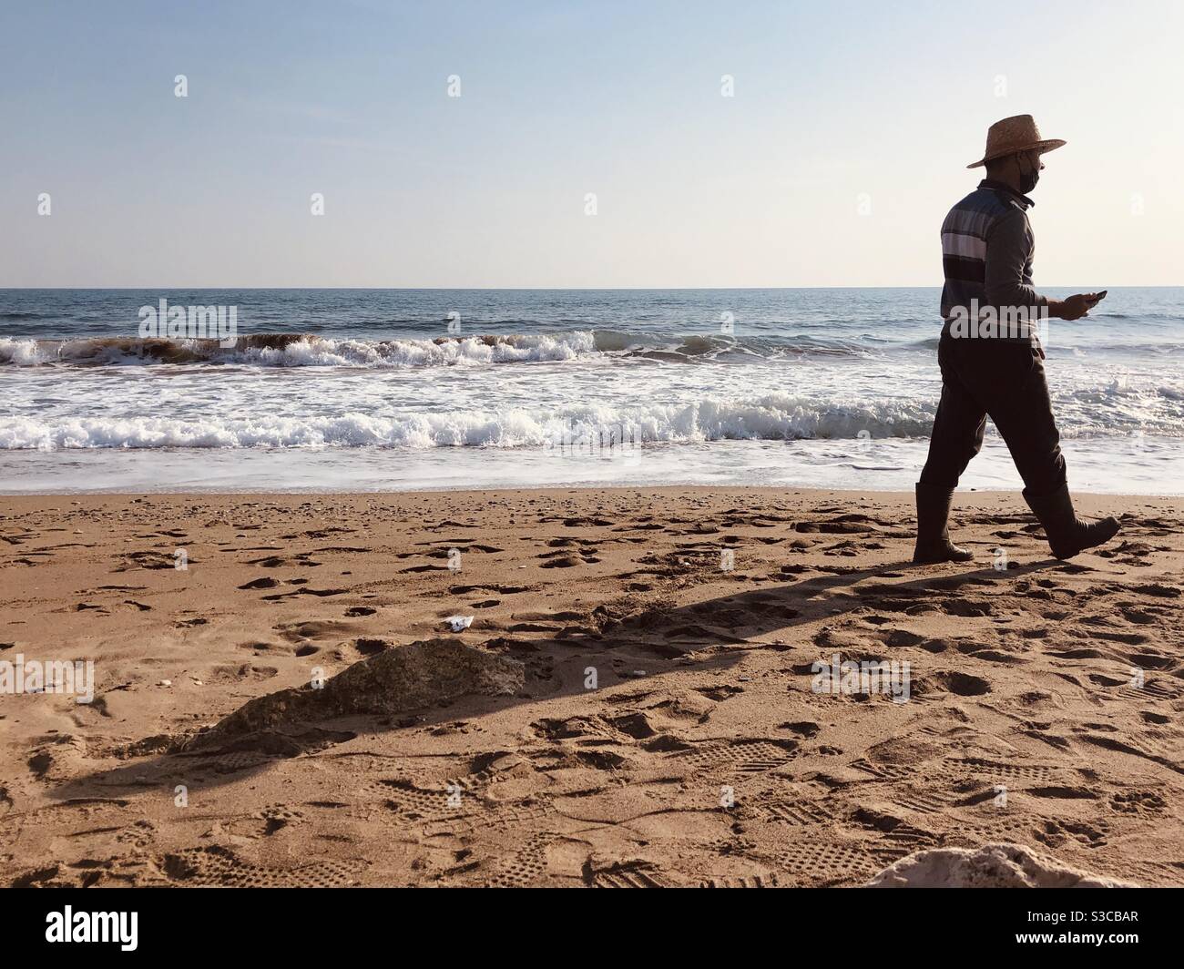 Man with a straw hat waking on the beach - Smartphone Captured Stock Image