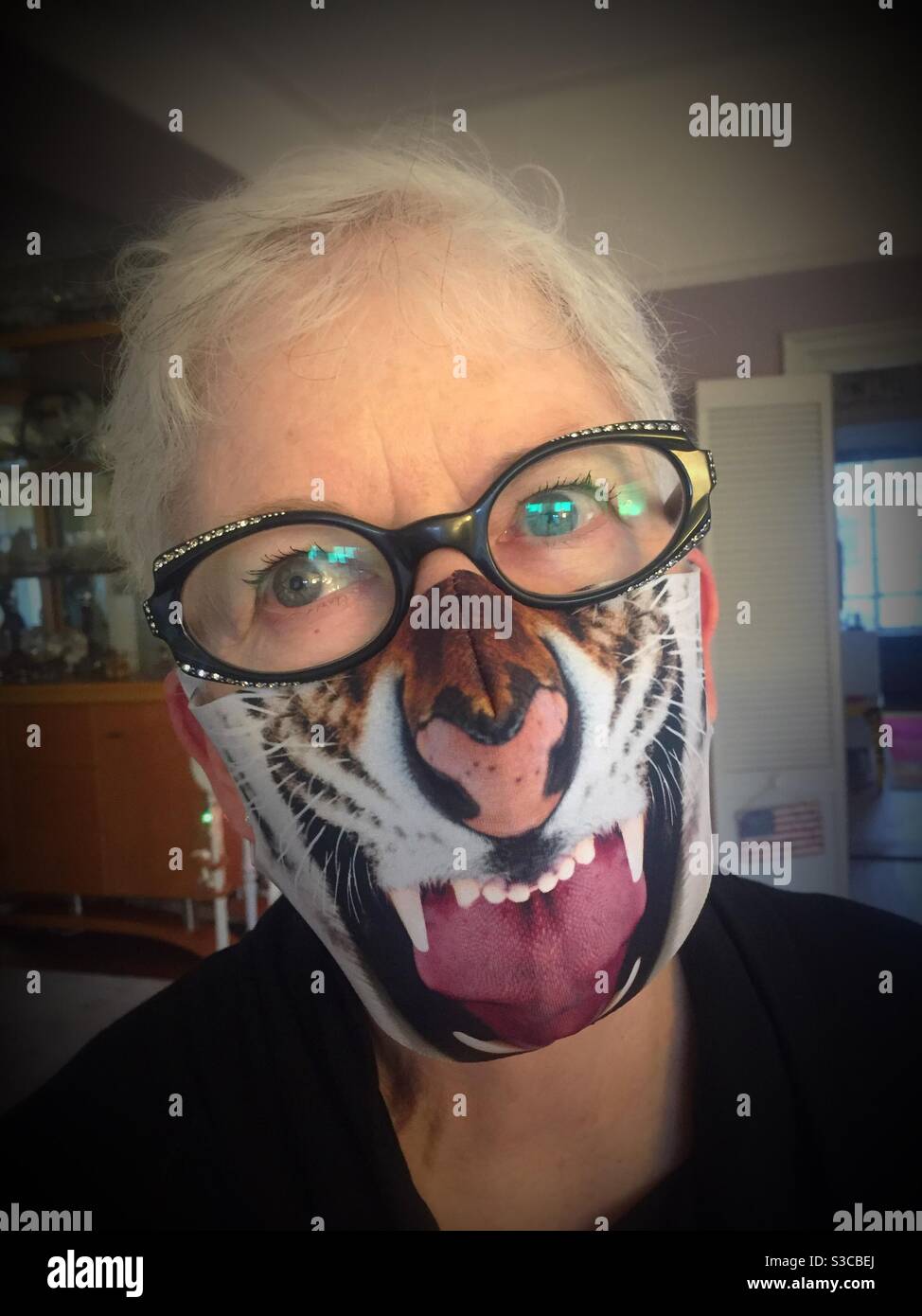 Senior woman looking at camera wearing a fierce tiger facemask, USA - Smartphone Captured Stock Image