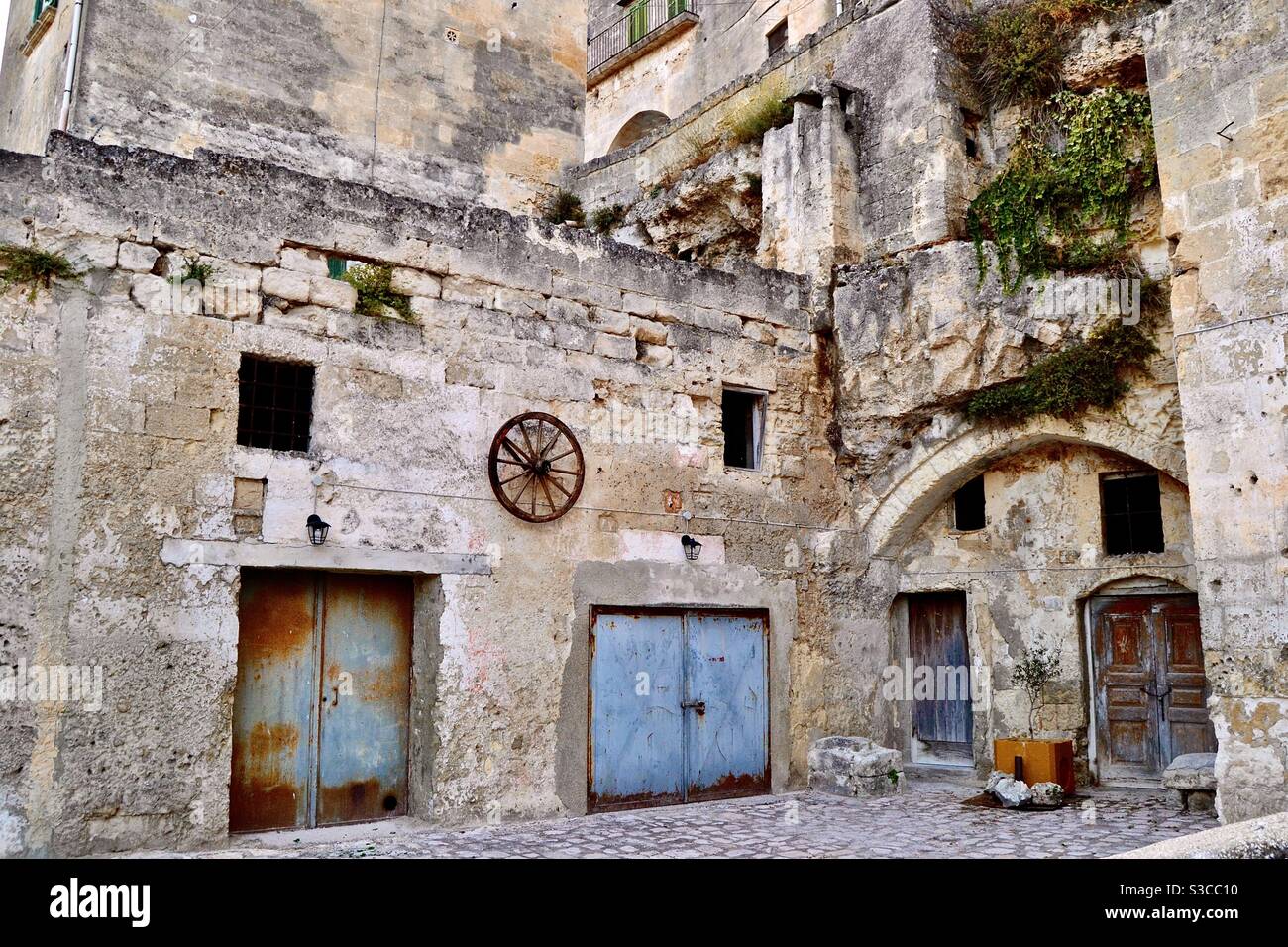 Ancient southern Italian rustic, atmospheric, residential, and romantic courtyard with rusty blue metal doors, small dark square windows and decorative iron cartwheel in Matera, Italy. Stock Photo