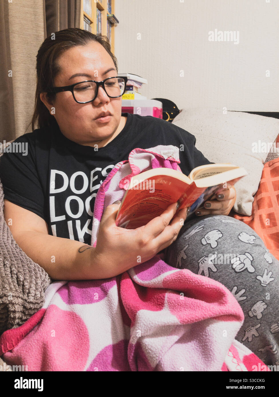 A lady sitting an reading a book at home. - Smartphone Captured Stock Image