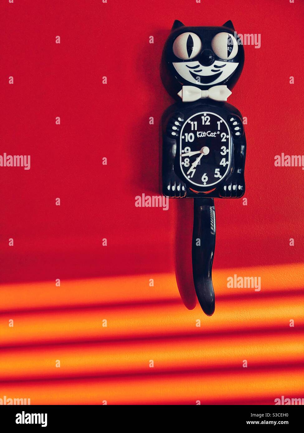 Kit Cat clock on red orange wall with lines of sunlight - Smartphone Captured Stock Image