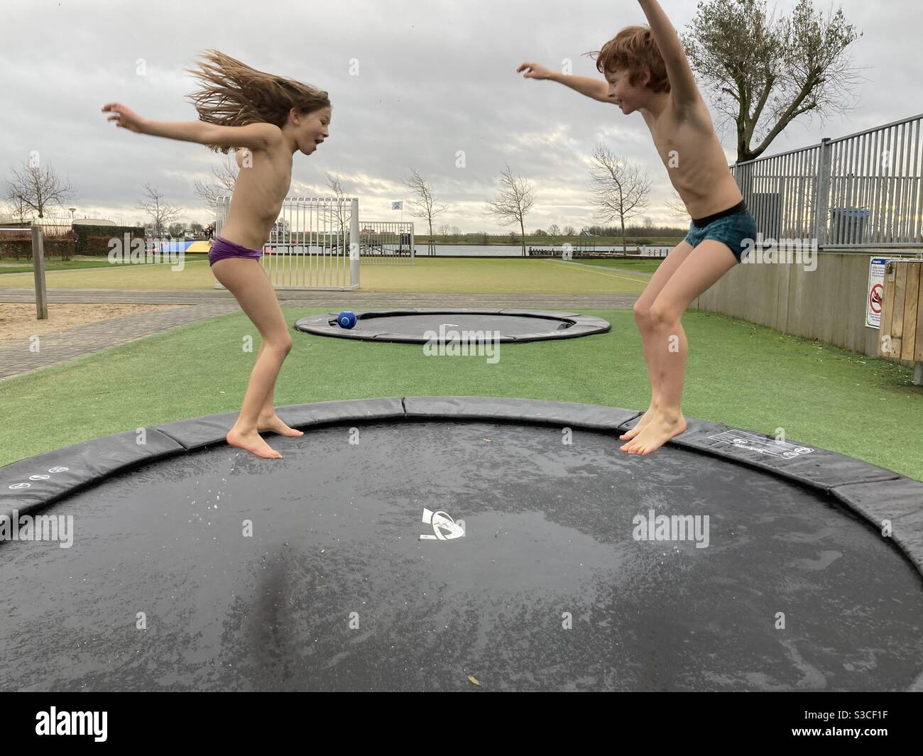Brother and sister jumping on a trampoline and enjoying themselves a lot Stock Photo