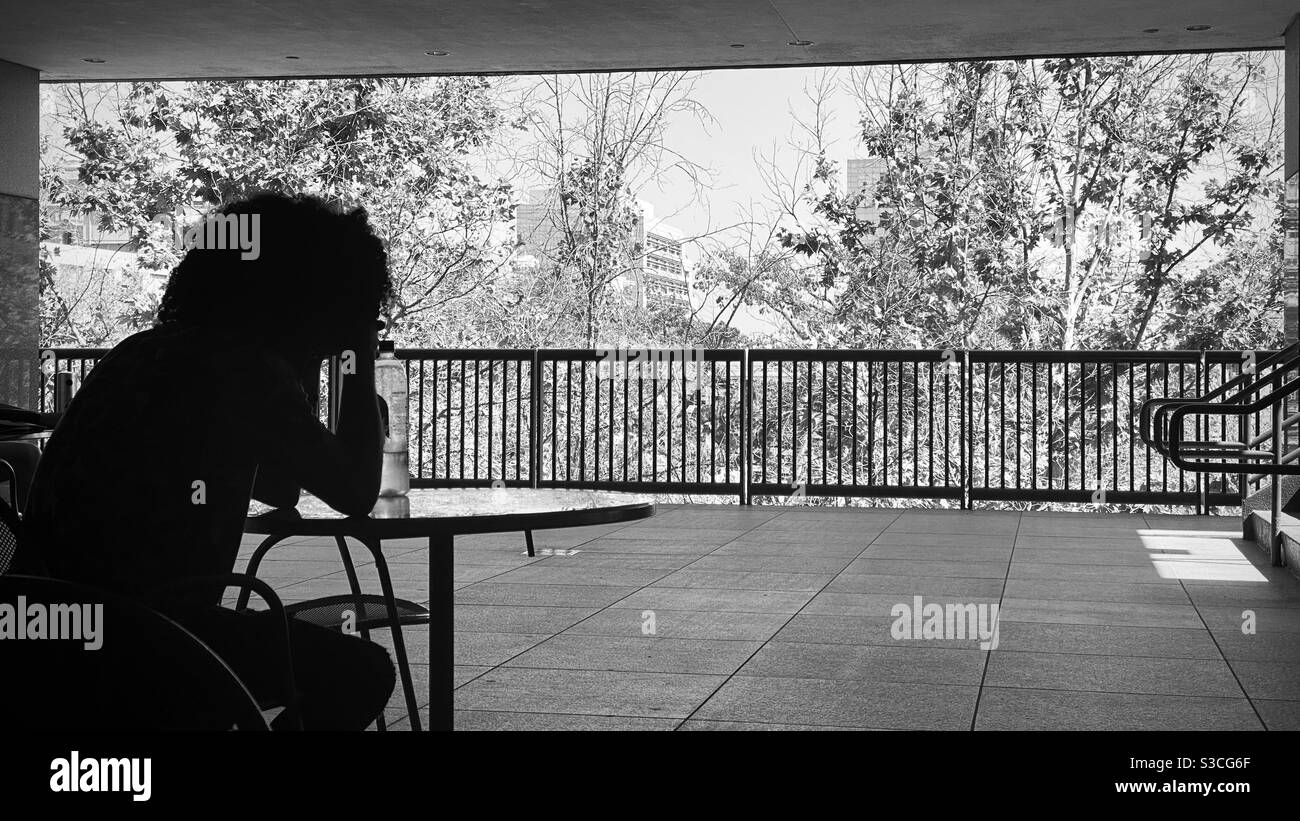 LOS ANGELES, CA, SEP 2020: Anonymous person sits with their head in their hands, silhouetted against a black and white cityscape, during Covid-19 pandemic - Smartphone Captured Stock Image