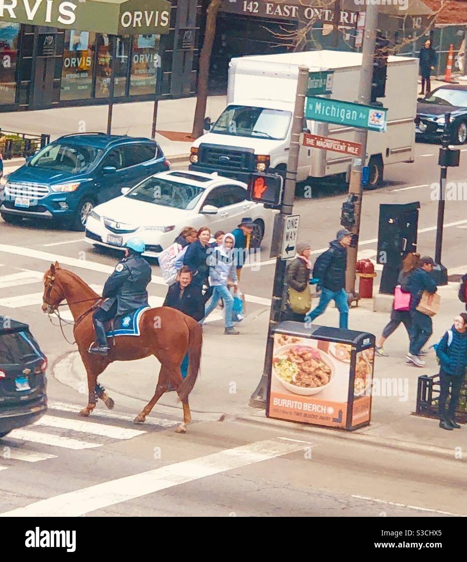 A policeman on a horse patrols the iconic Michigan Avenue, The magnificent mile, in Chicago Illinois USA Amid pedestrians and car traffic downtown - Smartphone Captured Stock Image