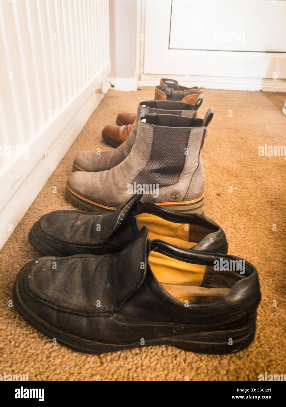 His and hers shoes lined up in a row in the hall. - Smartphone Captured Stock Image