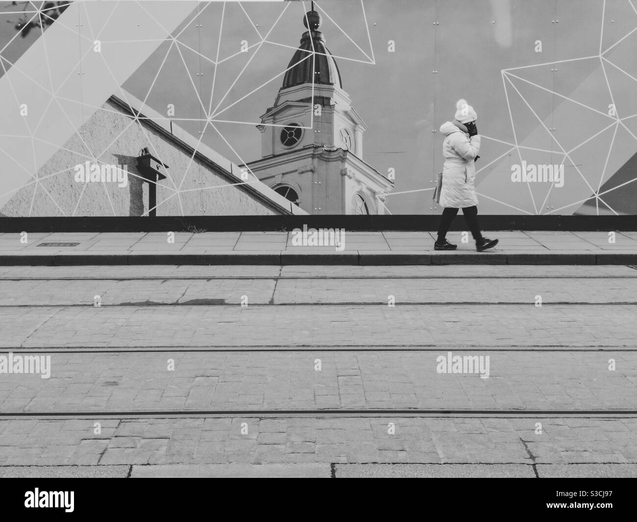 A person walks past a hoarding with an image of a church spire. - Smartphone Captured Stock Image