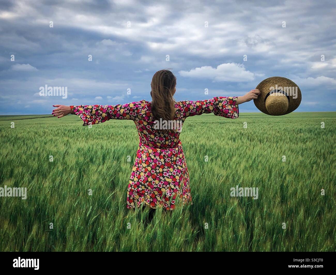 Woman wearing colorful dress and straw hat in a field of green wheat - Smartphone Captured Stock Image