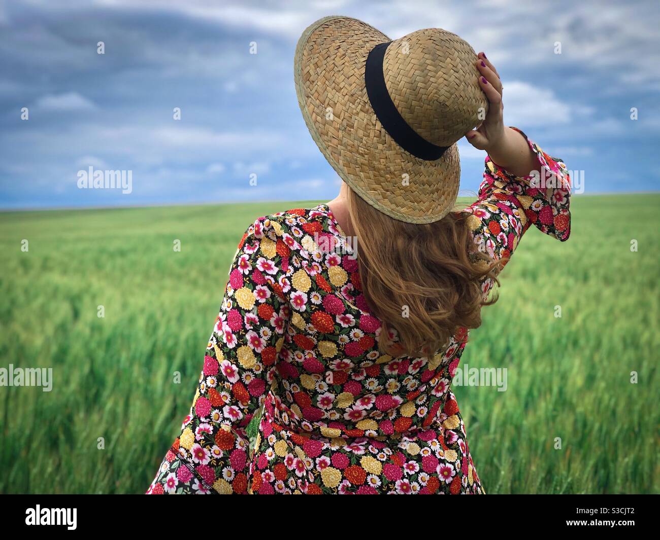 Woman wearing colorful dress and straw hat in a field of green wheat - Smartphone Captured Stock Image