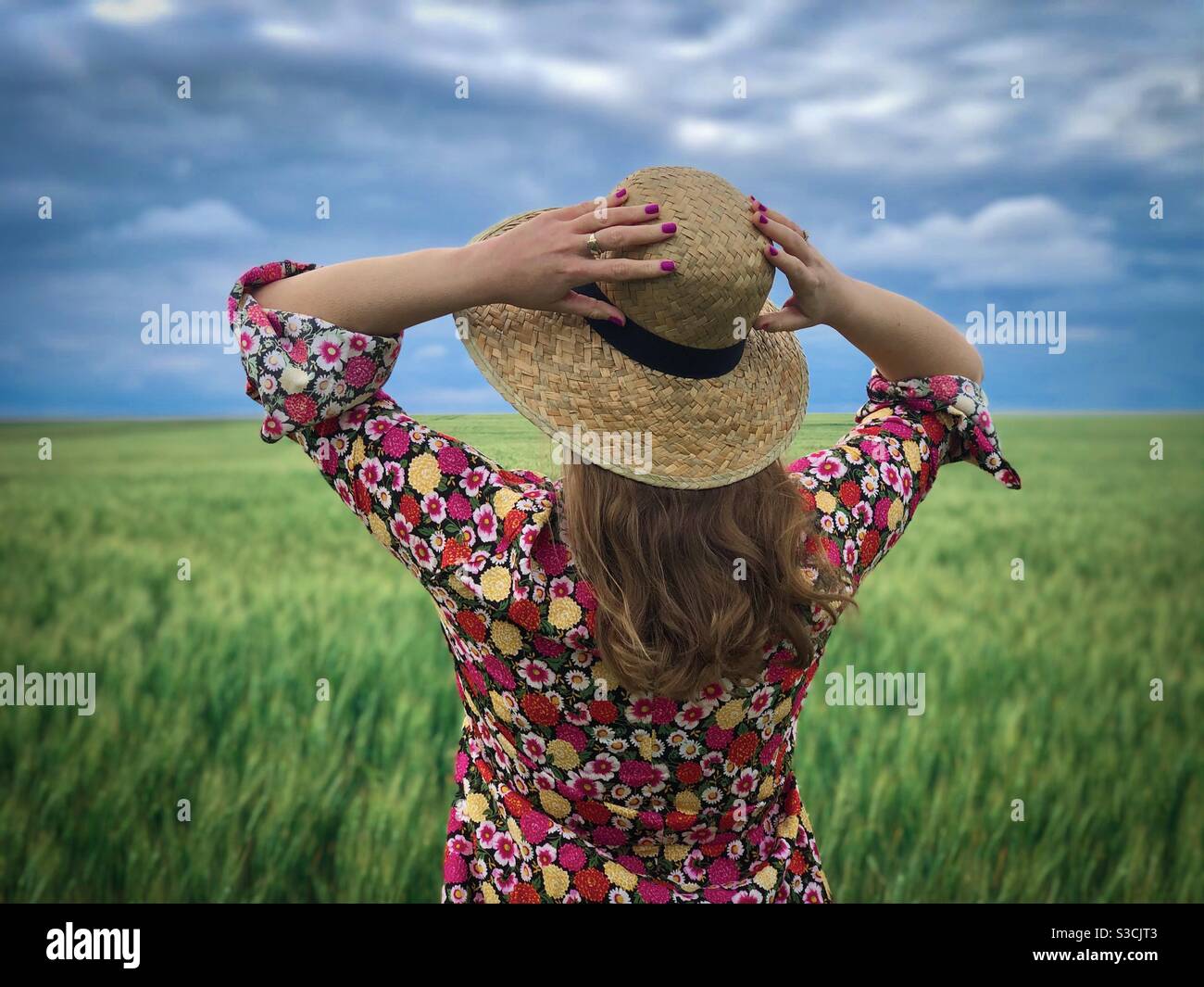 Woman wearing colorful dress and straw hat in a field of green wheat - Smartphone Captured Stock Image