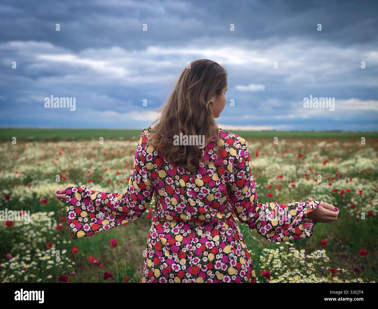 Woman wearing colorful dress standing near a field of poppies and daisies - Smartphone Captured Stock Image