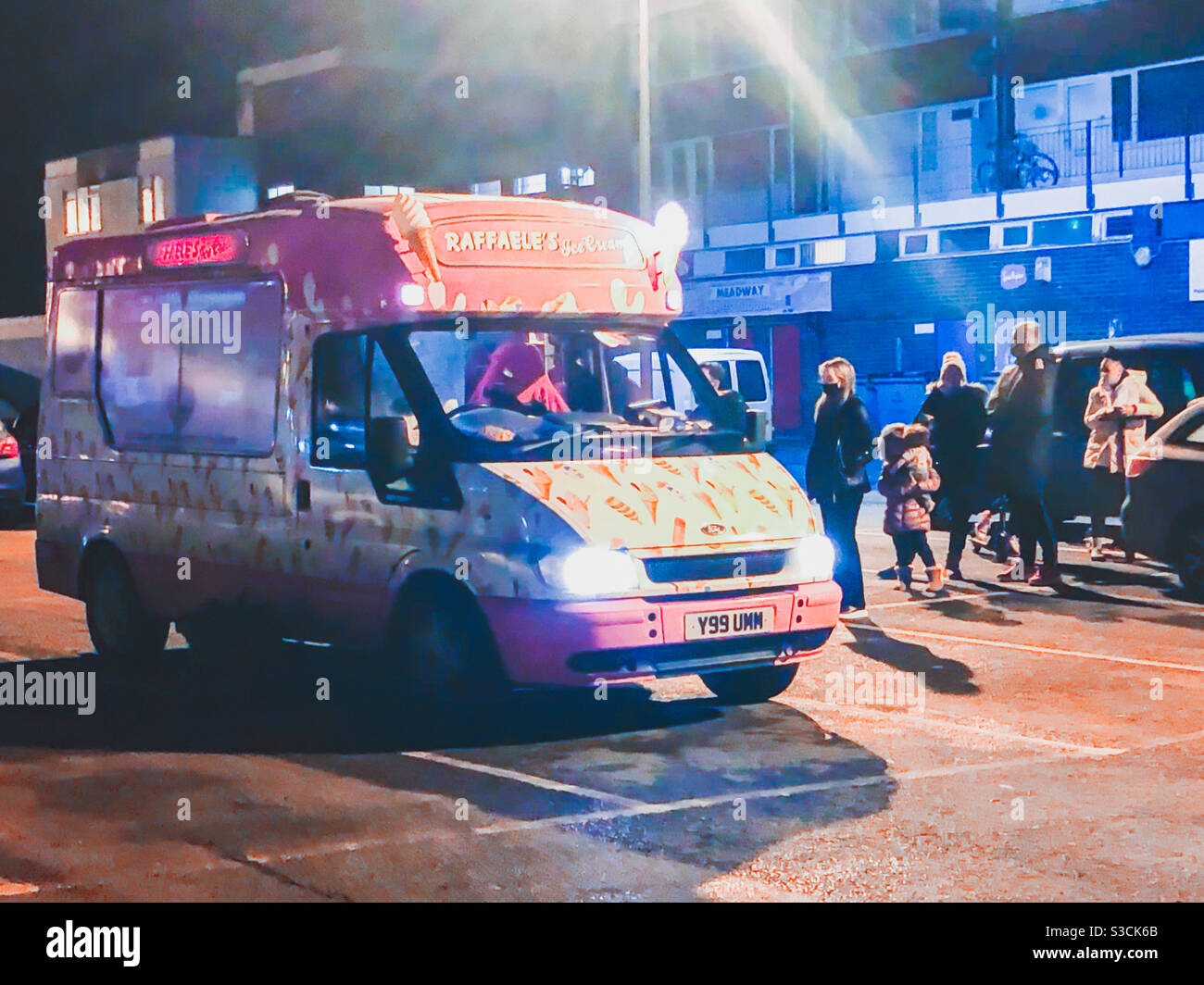 A queue of people at an ice cream van parked in a car park in the dark. - Smartphone Captured Stock Image