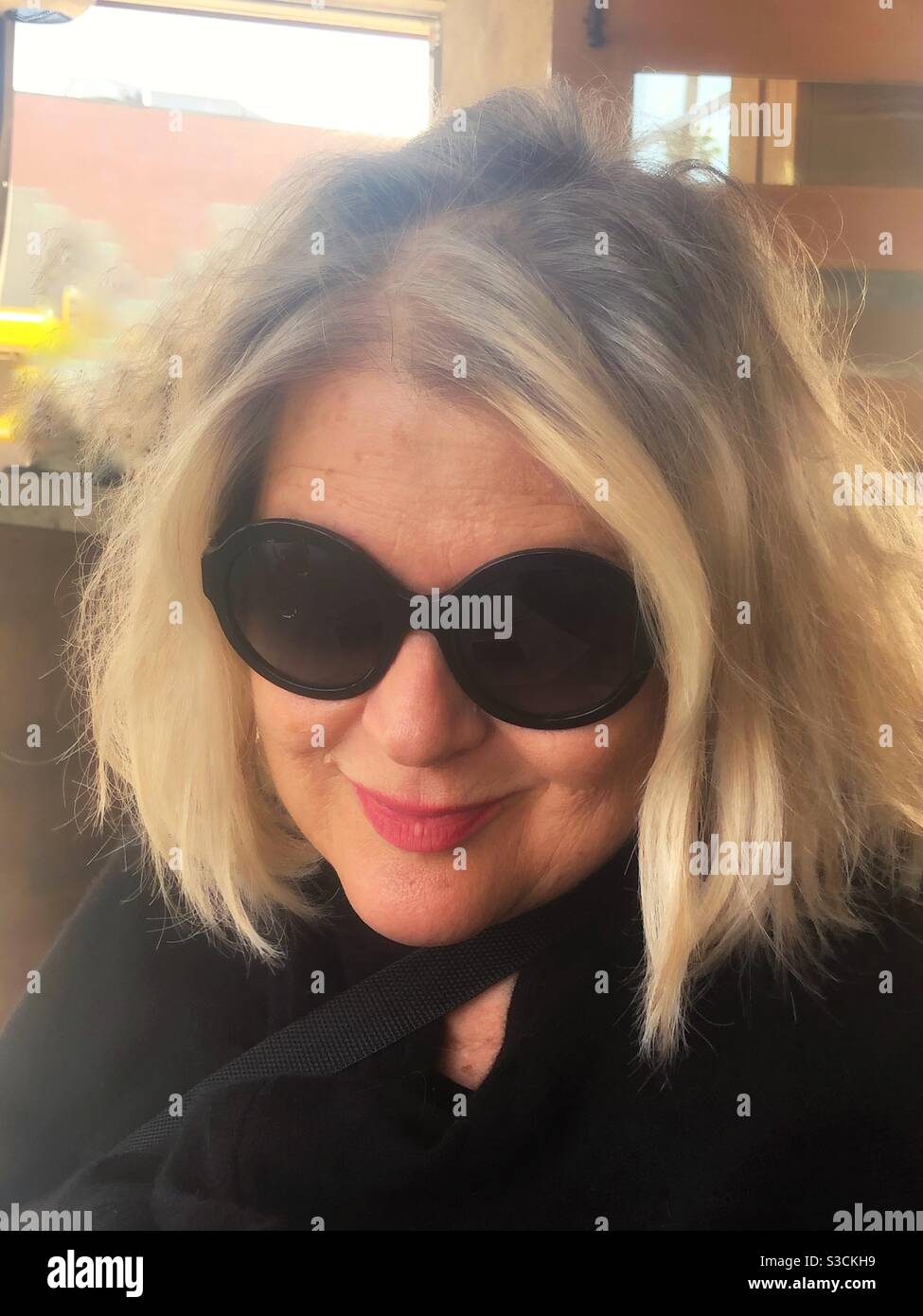 A beautiful blonde Southern California woman Smiles playfully behind large sunglasses In San Diego California, USA - Smartphone Captured Stock Image