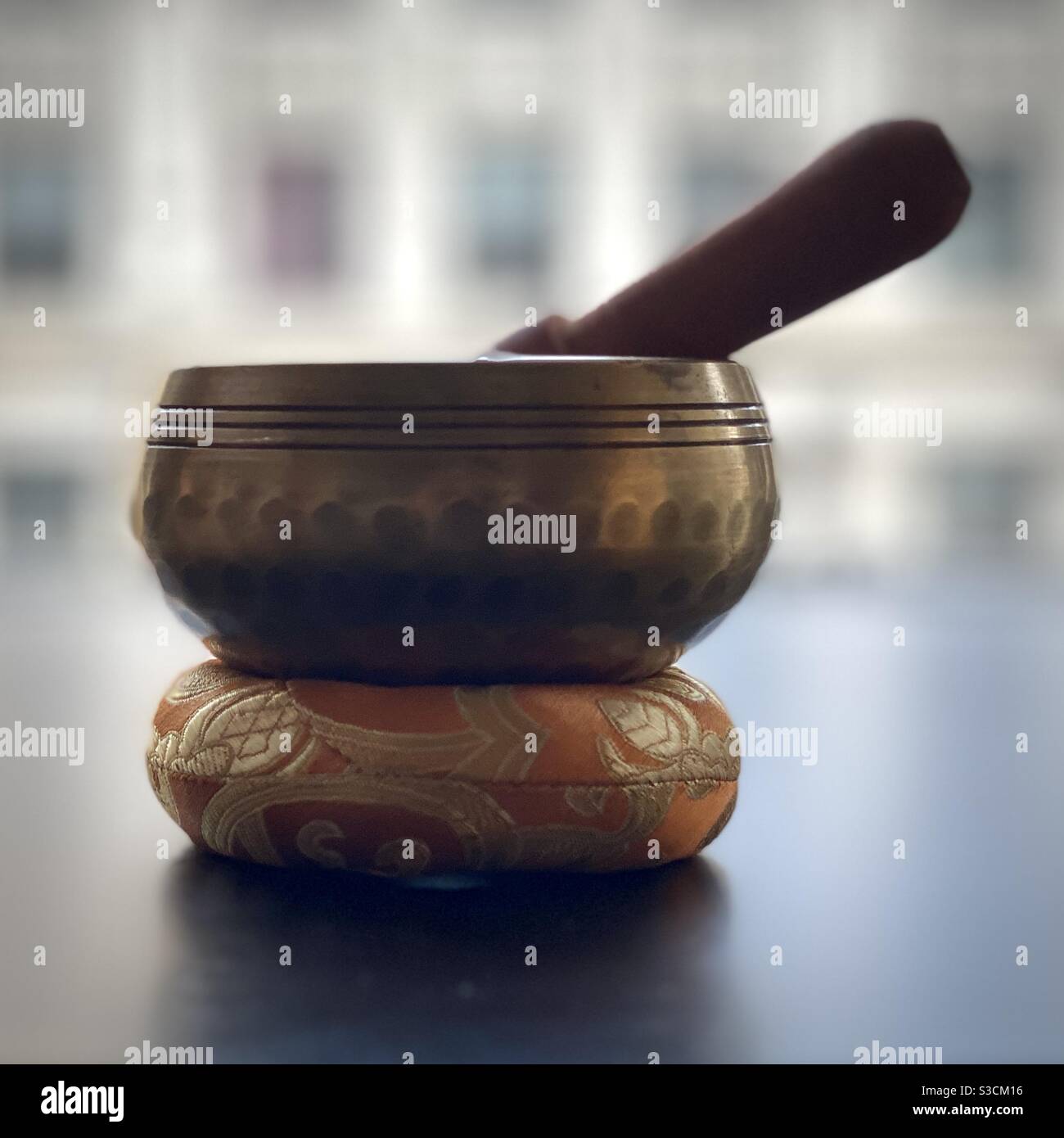 Chiming brass meditation bowl with wooden hammer on a small orange and gold cushion. Shallow focus. - Smartphone Captured Stock Image