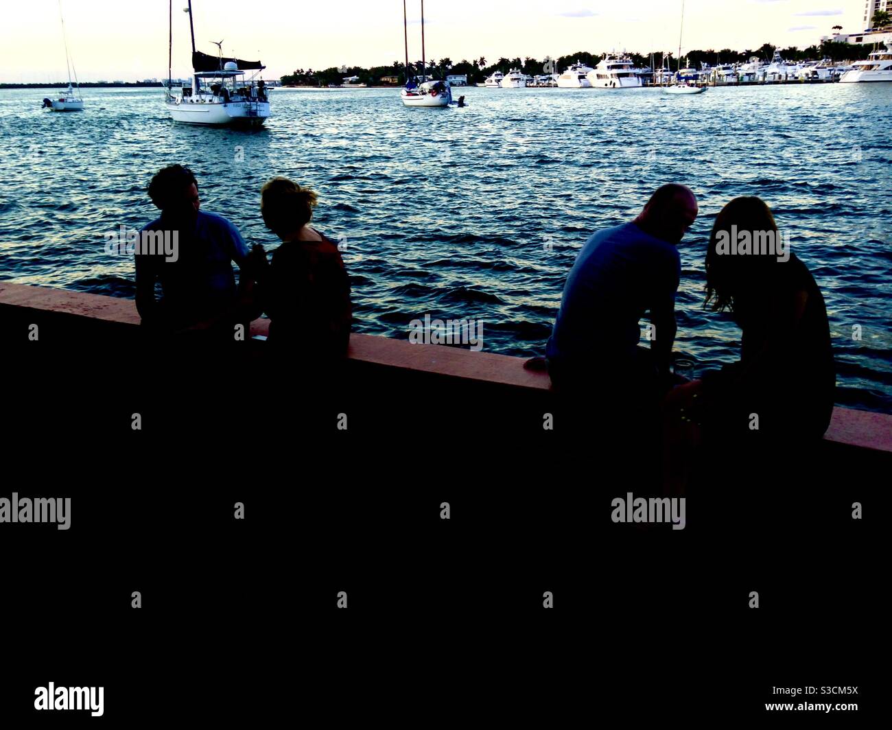 A lovers kedge by the ocean’s edge as couples watch boats in the blue water in South Miami Beach, Florida, USA. - Smartphone Captured Stock Image