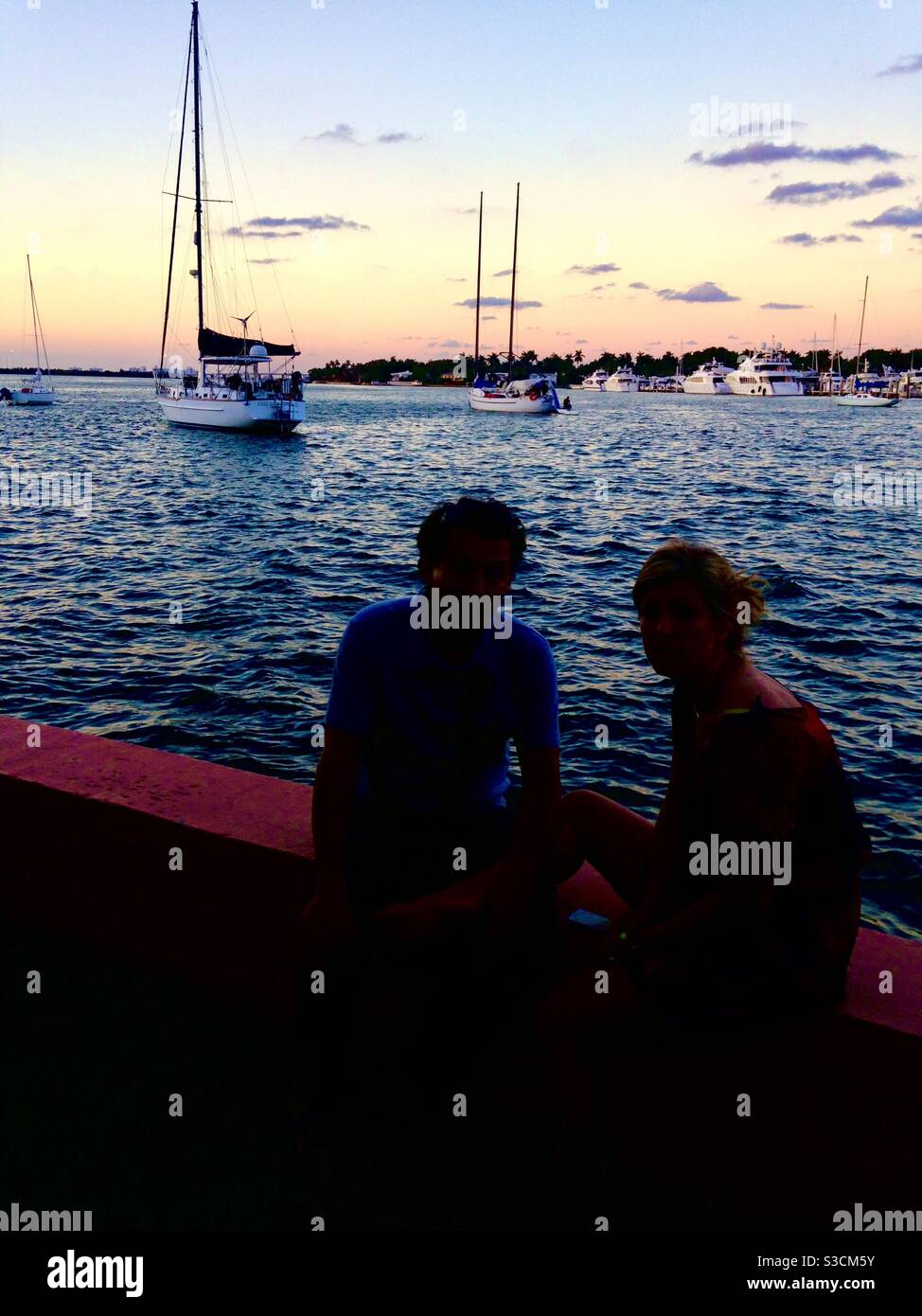 A loving couple takes in the beautiful sunset on the shores of South Miami beach as yachts and sail boats go by - Smartphone Captured Stock Image