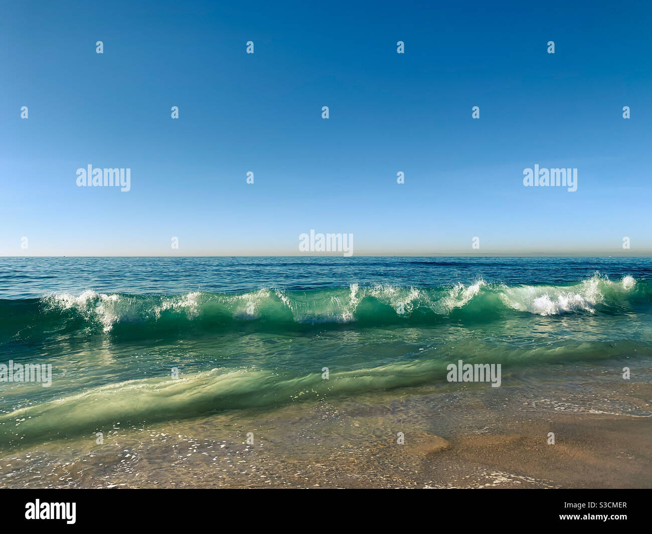 Waves crushing onto sandy beach on a clear sunny day. Stock Photo