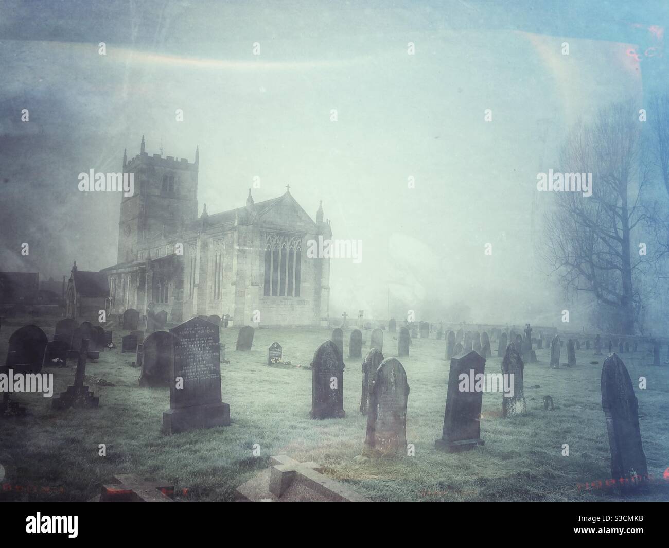A spooky graveyard scene with graves and church on a Misty or foggy day - Smartphone Captured Stock Image
