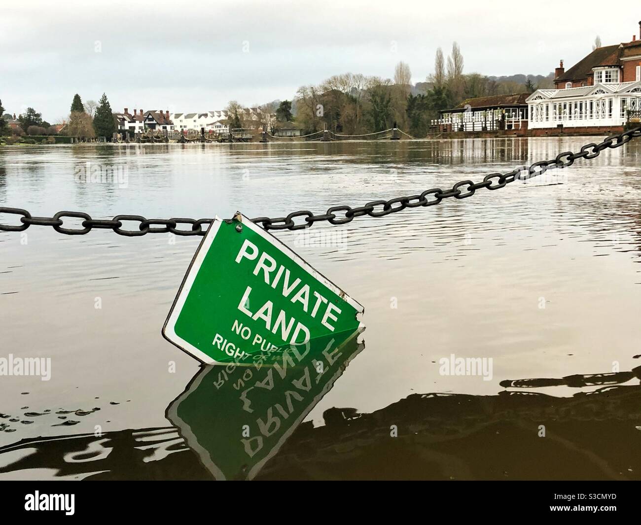 Green “Private Land” sign hanging semi-submerged in Thames suspended by metal link chain under Cookham Bridge,  England. Stock Photo
