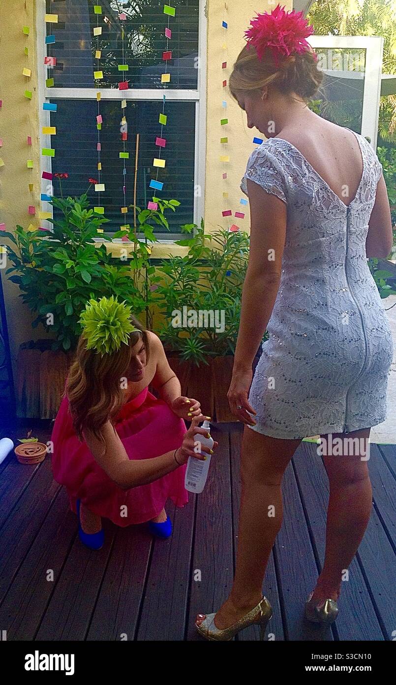 For an outdoor at home wedding in Miami Florida, the bridesmaid Sprays the bride with mosquito repellent! - Smartphone Captured Stock Image