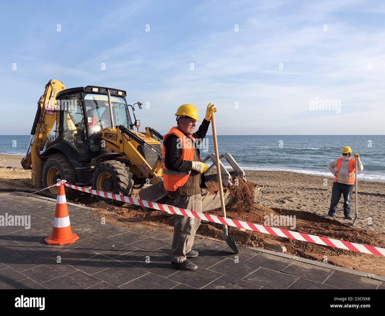 Construction workers and an excavator by the sea - Smartphone Captured Stock Image Construction workers and an excavator by the sea - Smartphone Captured Stock Image