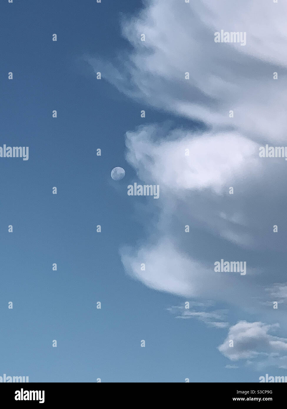 Surreal. Clouds reaching out to the moon in a dusky blue sky. Half frame of sky, half white clouds - Smartphone Captured Stock Image