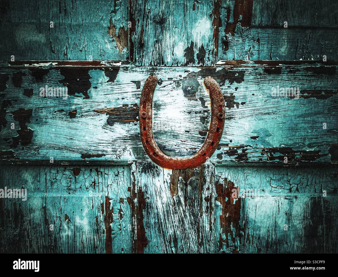 Old rustic horseshoe on wooden door with peeling blue paint Stock Photo