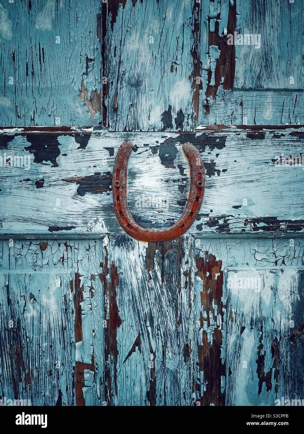 Old rustic horseshoe on wooden door with blue peeling paint Stock Photo