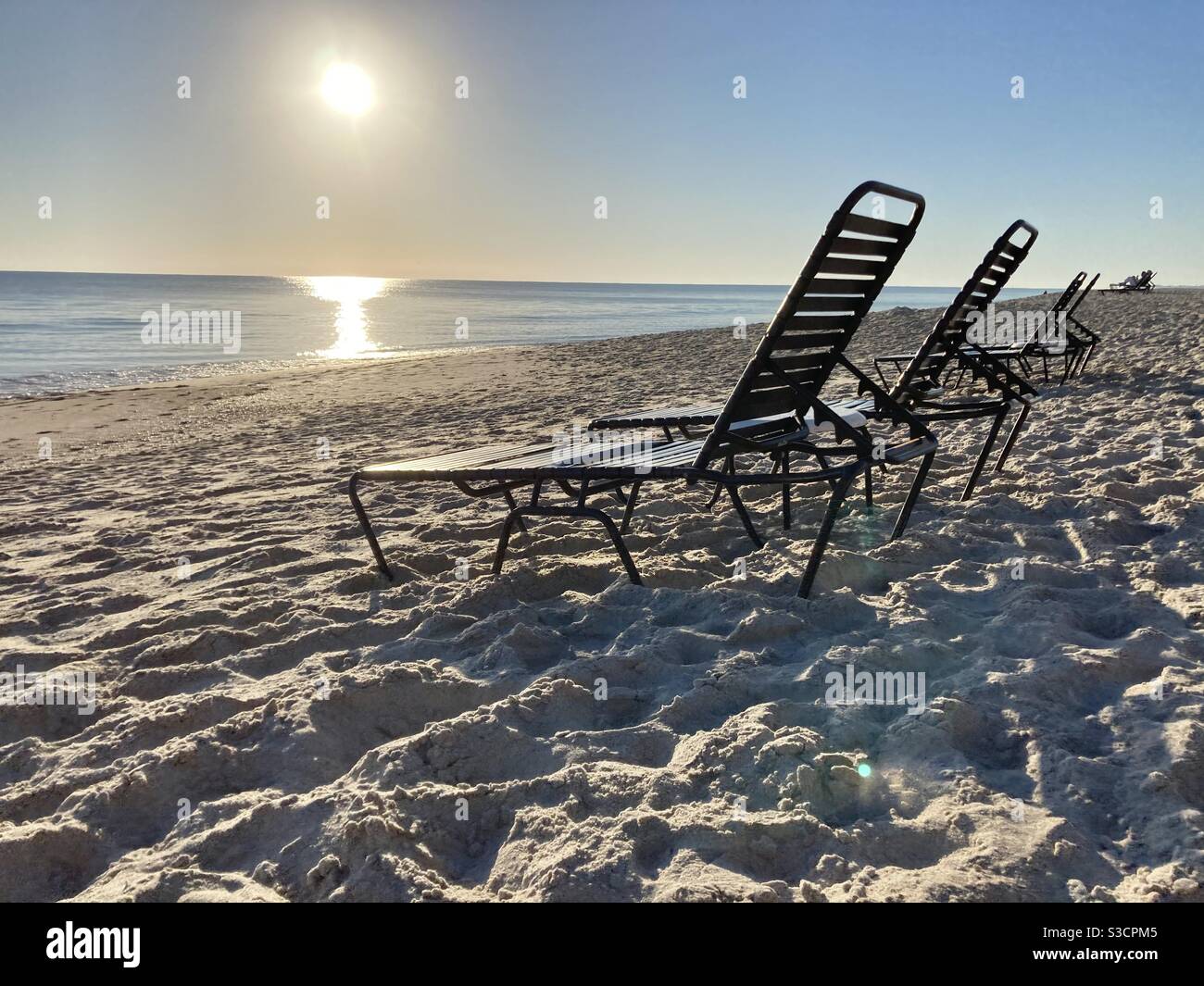 Empty beach chairs with the rising sun in the background it is very calm water, Hardly any waves - Smartphone Captured Stock Image
